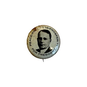 Puede incluir: Botón de campaña vintage con un retrato de un hombre con traje. El botón redondo tiene las palabras "PEACE • PROGRESS • PROSPERITY" y "FOR PRESIDENT" alrededor del borde. Tiene un alfiler en la parte posterior.