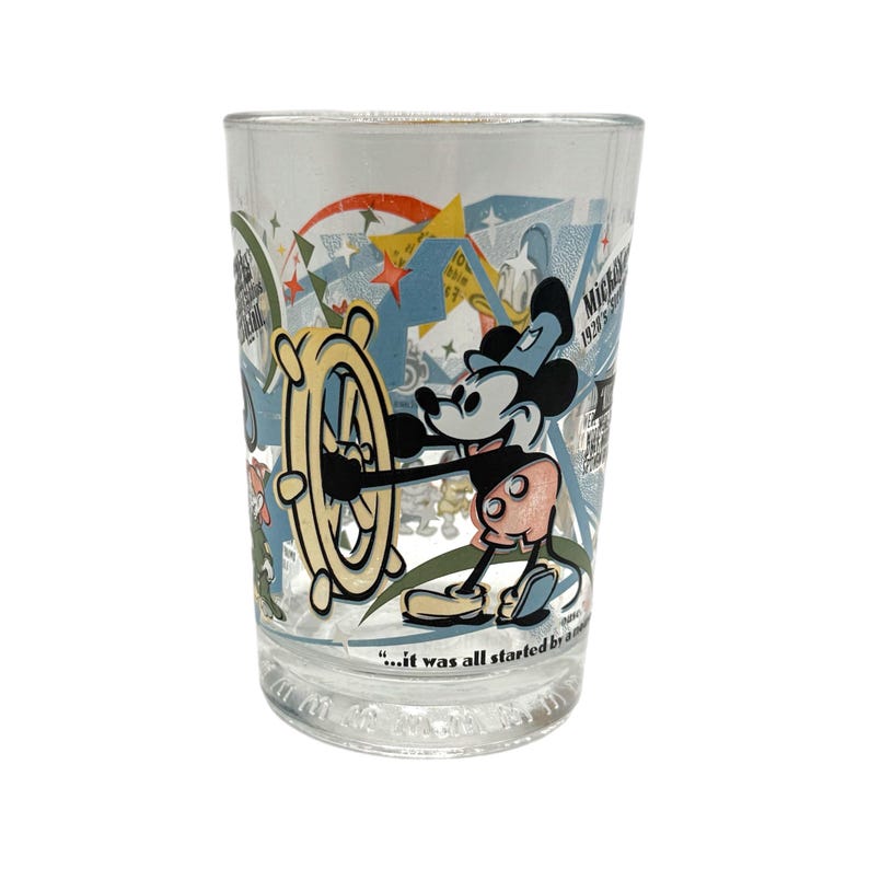 Puede incluir: Vaso transparente con una colorida ilustraci&oacute;n de Mickey Mouse al tim&oacute;n de un tim&oacute;n. El dise&ntilde;o incluye estrellas, texto y una cita. Un vaso coleccionable de estilo vintage.