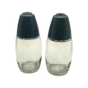 Può includere: Due saliere e pepiere in vetro trasparente con coperchi in plastica blu scuro. Le saliere e le pepiere hanno una forma ovale e sono vuote. I coperchi hanno piccoli fori.