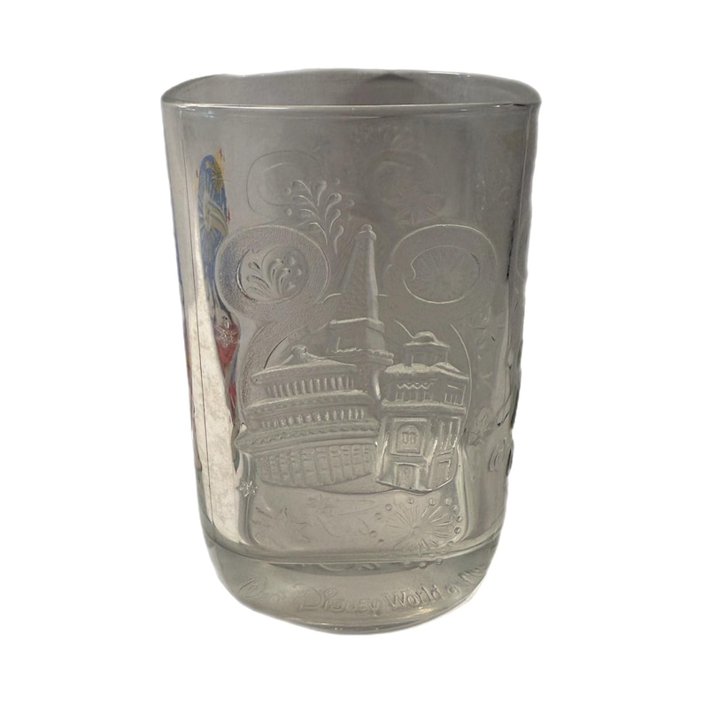 May include: Clear glass tumbler with etched images of buildings and floral designs. The tumbler features a detailed depiction of a building with a tall spire, and the words "Disney World" are etched at the bottom.