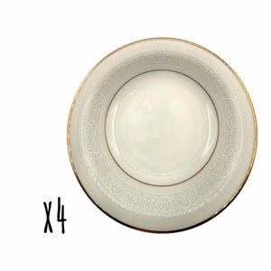 Może przedstawiać: Cztery białe talerze porcelanowe ze złotą obwódką i szczegółowym, wytłoczonym wzorem kwiatowym na krawędzi. Talerze mają centralny zagłębiony obszar. Liczba "x4" jest napisana czarnym pismem w lewym dolnym rogu.