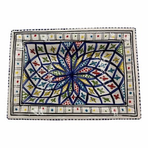 May include: Rectangular ceramic serving dish with a vibrant, geometric floral design. The dish features a white border with black and blue accents, and a central pattern in blue, yellow, red, and green. A decorative piece for serving food.