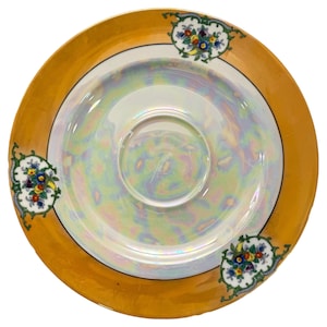 May include: A vintage iridescent saucer with a gold rim and floral accents. The saucer has a central indentation and is decorated with colorful flowers and green leaves. The gold rim is wide and the saucer is white in the center.