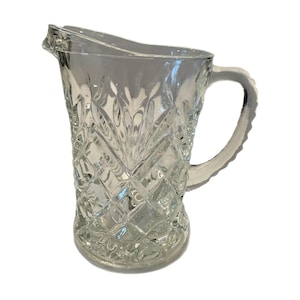 May include: A clear glass pitcher with a diamond pattern and a handle. The pitcher is empty.