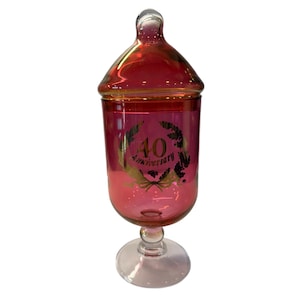 May include: A pink glass jar with a gold lid and a gold inscription that reads "40th Anniversary".