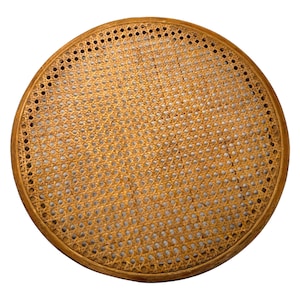 May include: A round, woven cane chair seat with a light brown wooden frame. The seat features a detailed, open weave pattern, and the frame has small, evenly spaced holes around the perimeter.