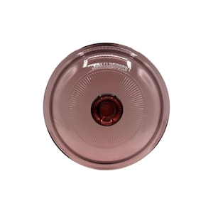 Puede incluir: Tapa de cristal circular transparente con un tinte malva. El centro presenta un pomo circular rojo oscuro. La tapa tiene un patrón acanalado que irradia desde el centro. El borde es negro. Vista desde arriba.