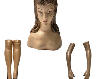Op de afbeelding: Een vintage mannequin hoofd, torso, armen en benen. Het hoofd heeft bruin haar en geschilderde gelaatstrekken. De torso en ledematen zijn geschilderd in een huidskleur. De benen dragen zwarte schoenen. Een klassieke display voor vintage kleding.