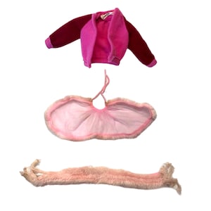 May include: A vintage doll outfit featuring a burgundy and pink jacket, a pink cape with a fur trim, and a pink fur stole. The jacket has a label that reads "Barbie". The outfit is designed for a doll.