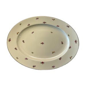 May include: An oval, off-white serving platter with a delicate floral pattern. Small clusters of pink and purple flowers are scattered across the surface and around the rim. The rim is trimmed with a thin, dark green line.