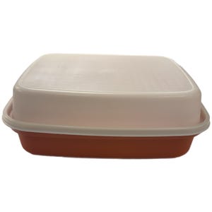 Op de afbeelding: Een rechthoekige voedselopslagcontainer met een wit deksel en een rood-oranje basis. Het deksel heeft een licht gestructureerd oppervlak en past goed op de basis. De container is ontworpen voor voedselopslag.