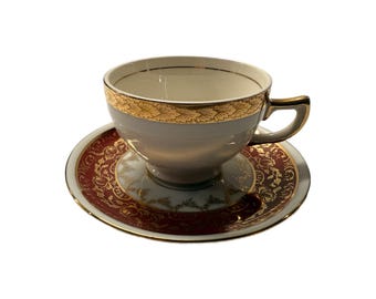 May include: A vintage teacup and saucer set. The cup is light gray with a gold rim and handle. The saucer is burgundy with a gold and white floral design. A classic addition to any tea set collection.
