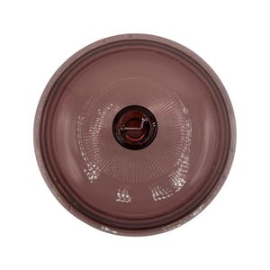 Puede incluir: Vista superior de un objeto de vidrio púrpura con un diseño circular. El objeto tiene un centro oscuro y un patrón acanalado que irradia hacia afuera. El borde exterior es un tono más oscuro de púrpura.