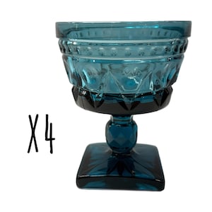 May include: Four teal-colored, vintage-style glass dessert dishes. Each dish features a square base, a faceted stem, and a bowl with diamond and beaded patterns. The text "X4" is in black on the left side.