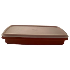 May include: A rectangular food storage container. It has a light peach-coloured lid and a reddish-orange base. The lid fits snugly over the base, creating an airtight seal. The container is made of durable plastic and is designed for food preservation.