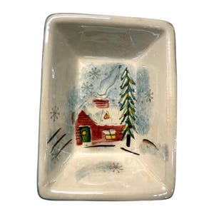 Könnte beinhalten: Rechteckige Keramikschale mit einer Winterszene. Das Innere zeigt ein rotes Haus mit schneebedecktem Dach, eine grüne Tür und ein gelbes Fenster. Ein grüner Weihnachtsbaum und Schneeflocken sind ebenfalls abgebildet. Die Schale hat eine weiße Außenseite.