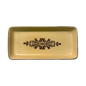 May include: Rectangular, light yellow ceramic dish with a brown floral design in the center. The dish has a slightly raised edge and a brown trim. The design is symmetrical and features stylized flowers and leaves.