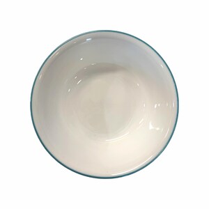 May include: A white ceramic bowl with a teal blue rim. The bowl is empty and has a glossy finish. The image is taken from a top-down perspective, showcasing the bowl's circular shape.