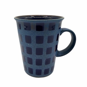 May include: A blue ceramic mug with a handle, featuring a grid pattern of dark blue squares. The mug has a slightly flared rim and a smooth, glossy finish. The mug is approximately 10 cm tall.