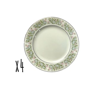 Puede incluir: Cuatro platos de cerámica blanca con un borde de estampado floral en rosa, azul y verde. Cada plato tiene un borde plateado. Los platos están colocados sobre un fondo blanco.