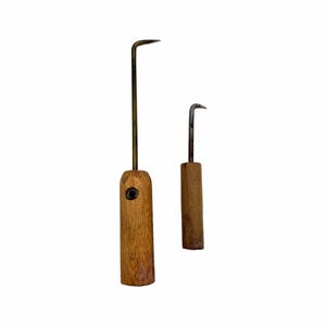 May include: Two metal hook tools with wooden handles. The larger tool features a long, thin, dark metal shaft with a right-angle hook at the top and a cylindrical wooden handle with a small dark circular inlay. The smaller tool has a shorter shaft.