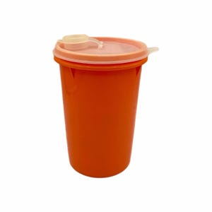 May include: A bright orange plastic storage container with a cylindrical body and a translucent, circular lid. The lid features a small, raised tab for opening and a central, slightly elevated circular section with a clear plastic seal.