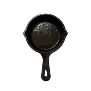 Pode incluir: Uma frigideira de ferro fundido preta com uma alça curta. A frigideira está vazia e tem uma superfície lisa e preta.