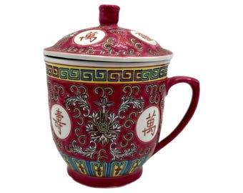 Puede incluir: Una taza de té de cerámica roja con tapa a juego. La taza presenta patrones florales y geométricos ornamentados en amarillo, azul y blanco. Se ven caracteres chinos en la taza y la tapa. La taza tiene un asa.