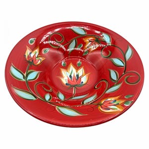 May include: A round, red ceramic serving bowl with a floral design. The bowl features hand-painted flowers in shades of orange, yellow, and red, with light blue leaves and green stems. The bowl is suitable for serving food.