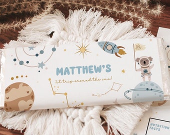 May include: A white chocolate bar wrapper with a space theme. It features a cartoon koala astronaut, planets, stars, and the text "MATTHEW'S it trip around the sun".