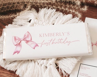 May include: A white chocolate bar wrapper with a pink bow and the text "KIMBERLY'S first birthday".