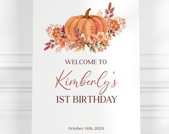 May include: Welcome to Kimberly's 1st Birthday sign with a watercolor pumpkin and floral design. The sign is white with brown text and is on an easel.