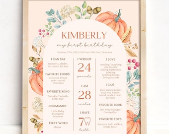 May include: A framed, personalized first birthday milestone poster. The design features a peach background with watercolor pumpkins, leaves, and floral accents. The poster includes the child's name, birthdate, weight (24 pounds), height (28 inches), and favorite things.