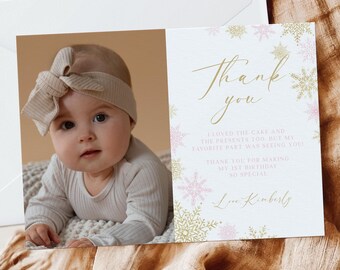 Puede incluir: Una tarjeta de agradecimiento blanca con un diseño de copo de nieve rosa y dorado. La tarjeta tiene una foto de una niña pequeña con una diadema beige y un mono blanco. El texto de la tarjeta dice "Gracias" y "Me encantó el pastel y los regalos también, pero mi parte favorita fue verte. Gracias por hacer que mi primer cumpleaños sea tan especial. Con cariño, Kimberly."