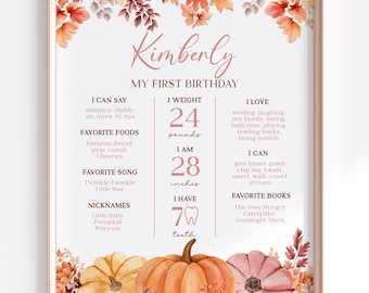 May include: A fall-themed first birthday chart for a baby named Kimberly. The chart features a watercolor illustration of pumpkins and autumn leaves. It includes details like weight (24 pounds), height (28 inches), favorite foods, songs, books, and other milestones.
