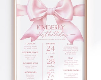 May include: Pink and white first birthday poster with a large pink bow at the top. The poster includes the name Kimberly, the date October 23rd, 2021, and details about the child's first year, including weight, height, favorite foods, songs, books, and nicknames.