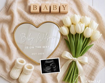 May include: A heart-shaped mirror with gold edging, inscribed with "Baby Wilson IS ON THE WAY OCT 2025", is next to a bouquet of white tulips tied with a cream ribbon. Knitted baby booties and a sonogram image complete the announcement.