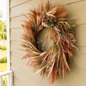 May include: A circular wreath constructed from dried grasses, wheat stalks, and foliage in shades of tan, brown, muted green, and burnt orange. The arrangement features a variety of textures with long, slender blades and feathery plumes.