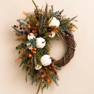 May include: A circular wreath constructed from brown woven twigs, adorned with an arrangement of artificial white pumpkins, green foliage, and clusters of small orange and dark berries. The decorative piece features a mix of textures and colors.