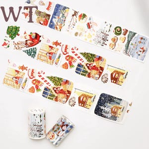 Op de afbeelding: Drie rollen washi tape met een winterthema. De tape heeft illustraties van een gezellige winterscène met een huis, een kerstboom en een sneeuwpop. De tape is wit met kleurrijke illustraties.