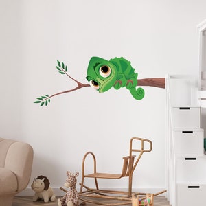 Peut inclure: Un caméléon vert aux grands yeux est perché sur une branche avec des feuilles vertes. Le caméléon regarde vers la gauche. L'autocollant mural est sur un mur blanc dans une chambre d'enfant.