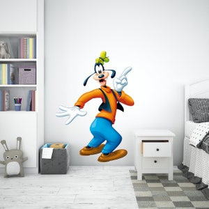 May include: A cartoon wall decal featuring Goofy, a Disney character, with a yellow hat, orange shirt, blue trousers, and white gloves. He is pointing with his right hand and smiling.