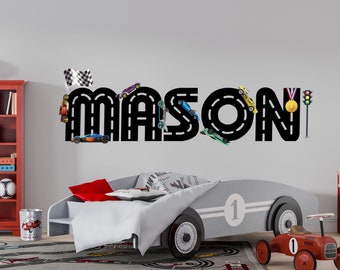 May include: A black and white wall decal with the name "MASON" spelled out in a racing track design. Toy race cars are placed on the track, and a checkered flag, a trophy, and a traffic light are also included in the design.