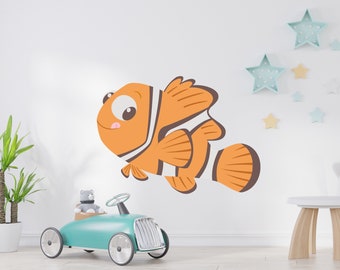 May include: A large orange and white cartoon clownfish wall decal. The fish has big eyes and is smiling. The decal is on a white wall, with a teal toy car and star-shaped decorations in the background.