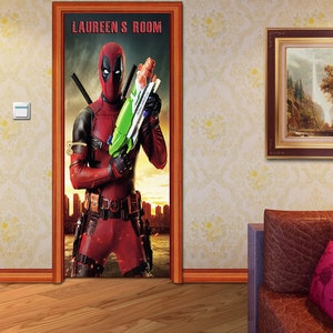 Op de afbeelding: Een deur sticker met een rood en zwart superhelden personage dat een groene waterpistool vasthoudt. De sticker heeft de tekst "LAUREEN'S ROOM" bovenaan.