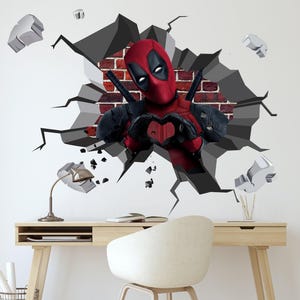 以下が含まれることがあります： 赤い黒のスーパーヒーローキャラクター、デッドプールがレンガの壁を突き破る。彼は両手でハートの形を作っている。壁はひび割れて壊れており、壁の一部が落ちている。