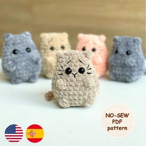 Könnte beinhalten: Fünf gehäkelte Amigurumi-Katzenspielzeuge in verschiedenen Farben, darunter Grau, Beige, Braun und Rosa. Die Spielzeuge sitzen alle auf einer weißen Oberfläche. Der Text "NO-SEW PDF pattern" steht unter den Spielzeugen. Das Bild zeigt auch zwei Flaggen, eine für die Vereinigten Staaten und eine für Spanien.