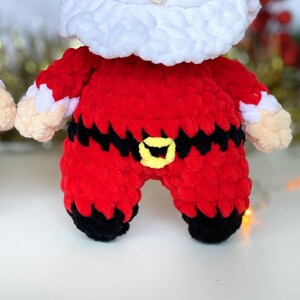 Puede incluir: Un mu&ntilde;eco de crochet de Pap&aacute; Noel con un traje rojo, un cintur&oacute;n negro y una hebilla amarilla. El mu&ntilde;eco tiene barba blanca y un gorro blanco.