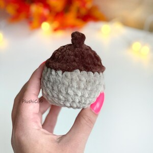May include: A handmade, plush acorn toy in shades of brown and gray. The acorn's cap is a dark brown, while the body is a lighter gray. The toy is soft and appears to be crocheted, perfect for fall decor or children's play.
