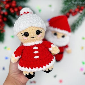 Puede incluir: Un conjunto de mu&ntilde;ecas de crochet de Pap&aacute; Noel y la se&ntilde;ora Claus. Las mu&ntilde;ecas est&aacute;n vestidas de rojo y blanco con ribetes blancos. Las mu&ntilde;ecas tienen ojos negros y caras sonrientes.